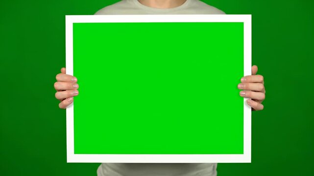 A person holding a white framed green sign in front of their body against a green background viewed from a straight-on perspective