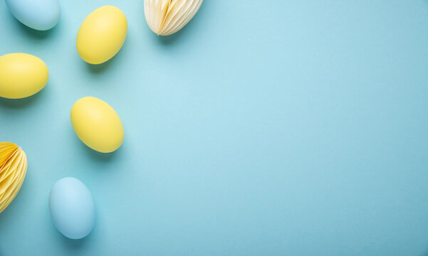 Happy Easter holiday background. Yellow and blue Easter egg decoration on light blue background top view.