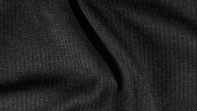 Black knit fabric seamless rotating motion background with wavy textile texture.