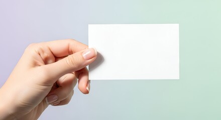 Obraz premium Close up of a manicured woman's hand holding a blank white rectangular card with a subtle shadow against a soft gradient background of purple and green hues