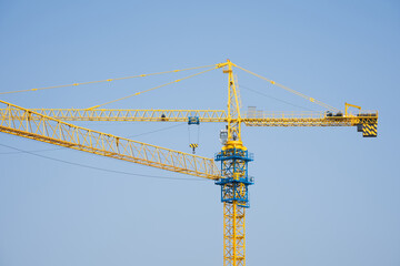 Yellow tower crane against clear blue sky at construction site with extended boom and lifting mechanism © zhu difeng