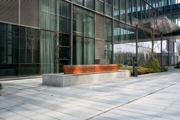 Modern office building with glass facade and wooden bench in outdoor plaza © zhu difeng