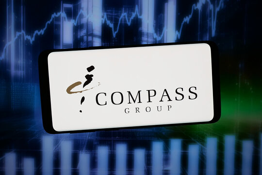 Stuttgart, Germany - 02-11-2026: In this photo illustration, the logo of British foodservice company Compass Group plc is displayed on a smartphone in front of abstract background on computer screen.