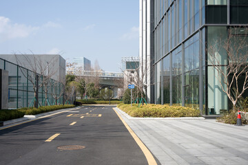Fototapeta premium Modern business park with glass curtain wall buildings, paved road, and landscaped greenery under clear sky