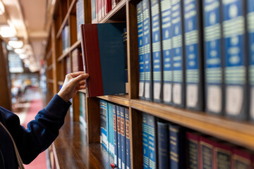 Hand selecting book from wooden library shelf. Legal research concept, attorney reference material, system study, academic knowledge and professional legislation archive. © Smallroombigdream