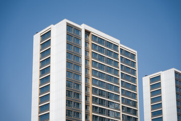 Modern white high-rise residential building with clean lines and glass windows against a clear blue sky