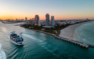 Fototapeta premium Container ship transporting cargo on Miami Beach. Cargo vessel with stacked shipping containers. Global trade concept with cargo. Container ship on ocean. Drone view of cargo shipping vessel.