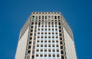 Fototapeta premium Unfinished high-rise building with scaffolding on facade against clear blue sky