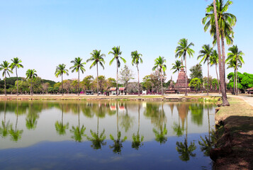 Obraz premium Ancient chedi and palms near pond, Sukhothai historical park, Thailand. Picturesque landscape with stone stupa in Sukhothai old city, Northern Thailand. Topic of vacation, travel, trip, cruise, tour