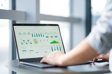 Person working on data analysis using a laptop with charts and graphs displayed on screen in an...