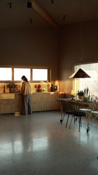 Woman slowly walking through a modern minimalist kitchen and drinking coffee. Warm natural light, contemporary interior design and calm atmosphere in a mountain house. Slow living and peaceful