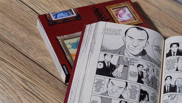 South Kalimantan, Indonesia - 02 16 2026 : Open Naoki Urasawa Monster manga showing black and white comic panels while other volumes rest behind on wooden surface.