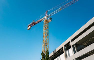 Fototapeta premium Construction crane over urban development site, bright blue sky.