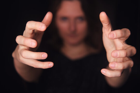 Woman with outstretcched hands on a dark background holding or grabbing an imaginary object or interacting with virtual reality and technology.