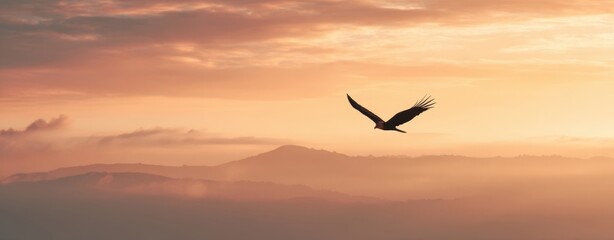 Fototapeta premium The bird soaring above layered mountains at golden sunrise with dramatic cloudy sky