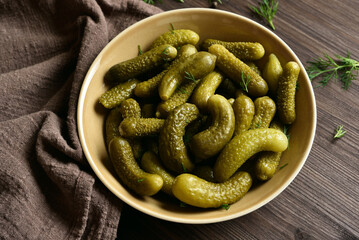 Pickled cucumbers in bowl on wooden background