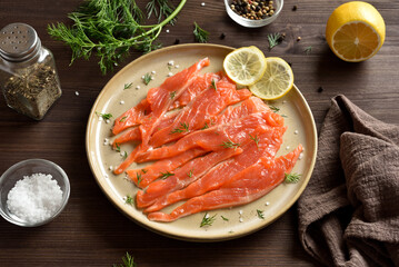 Slices of salted salmon on plate on dark wooden table