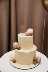 Festive two-layer cake with a candle on top stands on a table against a curtain background