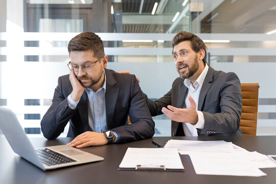 Upset businessman in a suit having a conversation with a colleague reassuring him, showing support and empathy for his burnout and stress in a modern office meeting room