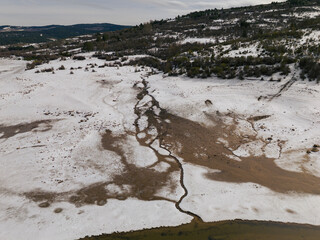 Aerial view of a thin water stream carving through sediment and snow in a high-altitude mountain valley