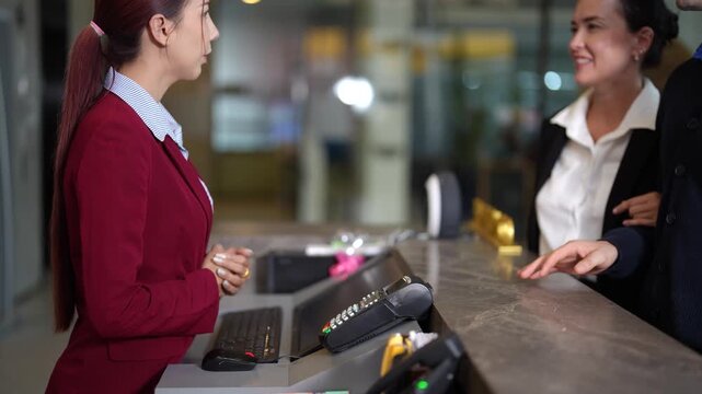 Man and woman arriving at hotel front desk, completing check in procedure and making credit card payment. Reception staff provides service before guests leave counter. Travel and accommodation theme.