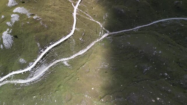 Drone video over hiking trails on Sennes Plateau in South Tyrol Italy, camera lifts from winding tracks and rocky pasture to a wide Dolomites panorama with slopes and cloud shadows