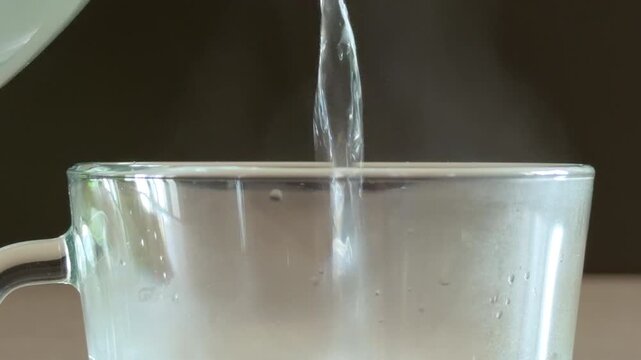 Hot water streams from a kettle into a clear glass mug. The liquid creates a rhythmic sloshing and splashing sound as the cup fills.