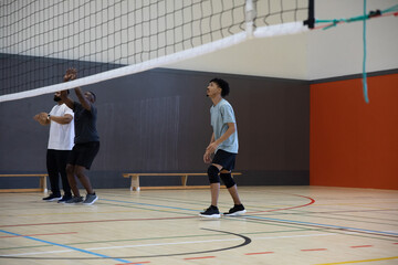 Teen male crouching on gym volleyball court near net wearing knee pads and sneakers, copy space