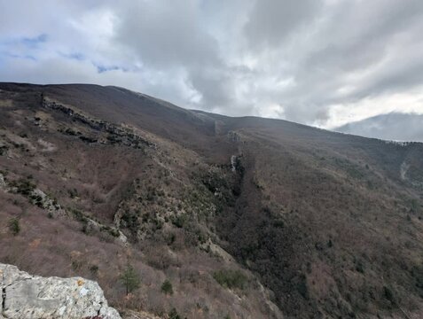 Panorama montano con una valle profonda che attraversa il paesaggio, caratterizzato da pendii ripidi e vegetazione rada tipica della stagione invernale