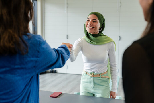 Diverse female professionals shaking hands in modern meeting room with red smartphone on table