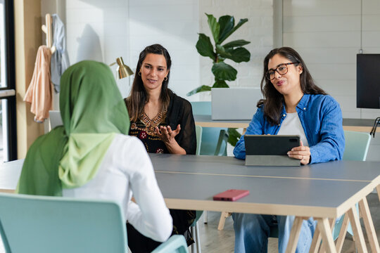 Diverse panel of women conducting interview in office meeting room using tablet and red smartphone