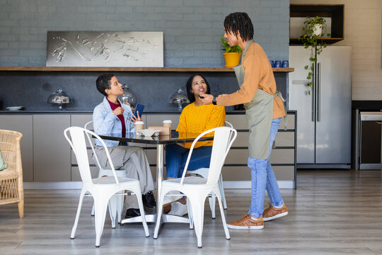 African American barista serving coffee to friends checking smartphone at cafe table, copy space