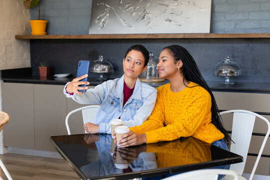 African American female friends taking selfie with smartphone holding coffees in coffee shop