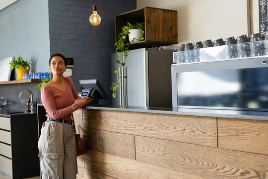 African American woman tapping payment terminal while holding reader at modern coffee shop counter