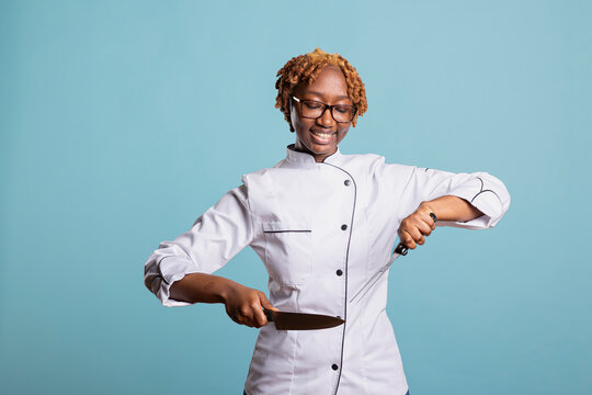 Smiling professional cook stands confidently against isolated background, holding knife and meat fork. Happy woman chef demonstrates culinary expertise, showing pride in cutting skills and cooking.