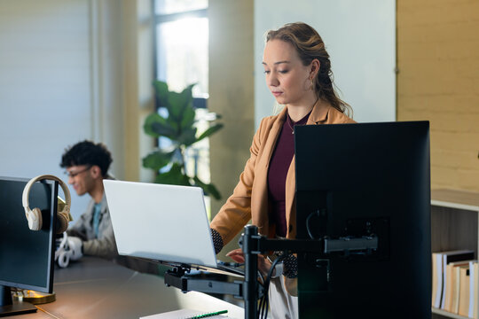 Diverse coworkers working at standing desk in office and typing at computer near plant, copy space