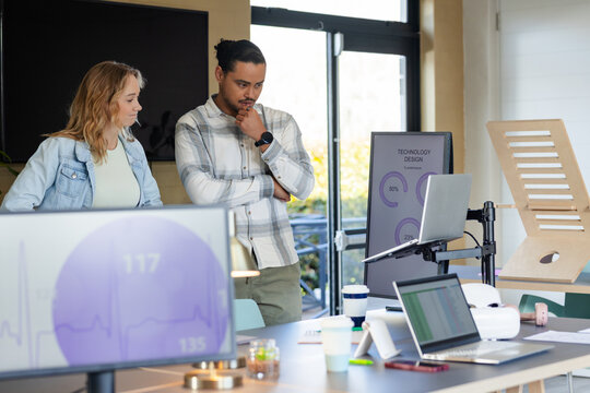 Diverse coworkers leaning over laptop on stand analyzing circular progress charts at modern office
