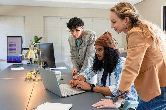 Diverse coworkers in casual attire collaborating around laptop at office table with coffee cup