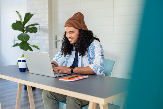 African American man sitting at desk working on laptop in home office with coffee cup