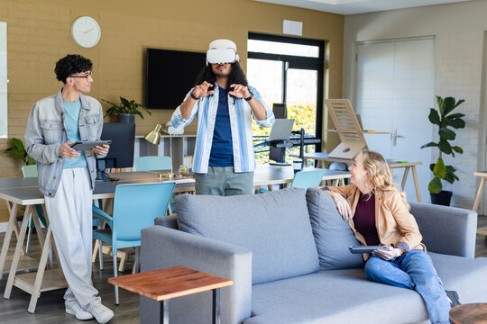 Diverse coworkers exploring virtual environment in lounge area using VR headset and tablets