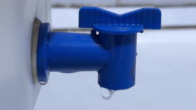 A blue plastic faucet on a white canister leaks slowly into a bathtub. Single water droplets fall and hit the surface below, creating a steady, rhythmic plinking and light splashing sound.