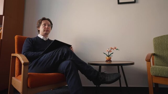 A young man sits in a chair and takes notes during a conversation. Conversation in a cozy office and an effort to understand the other side.