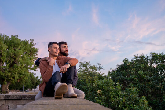 Affectionate gay couple sitting on a wall at sunset