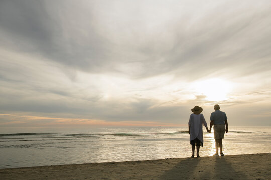 Back view of senior couple standing hand in hand on the beach watching sunset, Liepaja, Latvia