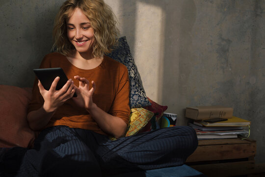 Portrait of smiling young woman sitting on bed using E-book reader