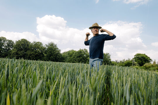 Confident man flexing muscles against cloudy sky in field