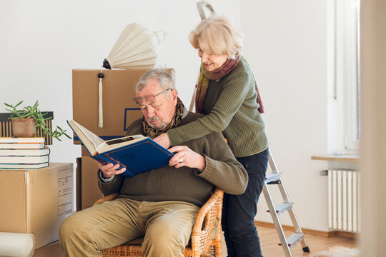 Senior couple looking at photo album surrounded by cardboard boxes in an empty room
