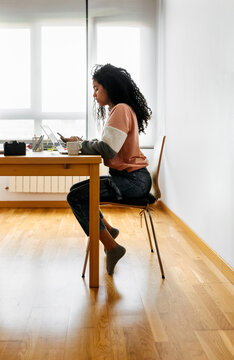 Young woman working from home using laptop and smartphone