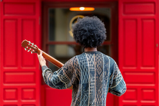 Young man playing guitar while standing in front of building