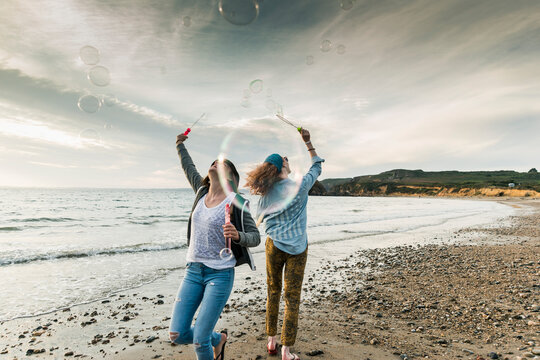Happy friends making soap bubbles on the beach